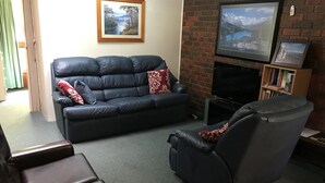Una sala de estar con un sofá de cuero negro, un sillón reclinable, un televisor de pantalla plana y una chimenea.