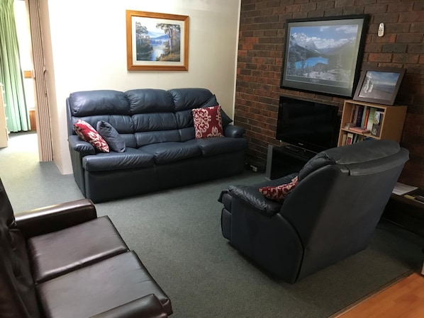 A living room with a black leather sofa, a recliner, a flat-screen TV, and a fireplace.