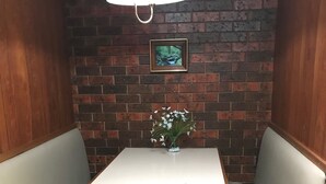 Un reservado en esquina con una mesa y dos bancos acolchados, una lámpara colgante y un cuadro en la pared de ladrillo.
