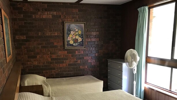 Un dormitorio con dos camas, una pared de ladrillo, un cuadro, un aparador y una ventana con cortinas.