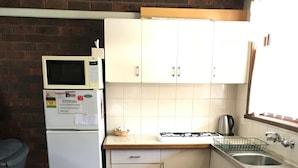 Cocina compacta con refrigerador, microondas, estufa, pileta y alacenas de madera.