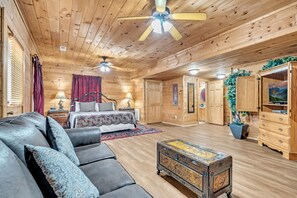 A log cabin interior with a large bed, a sofa, a chest of drawers, and a ceiling fan.