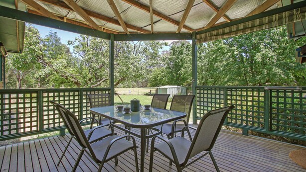 A covered outdoor seating area with a table and chairs, surrounded by a wooden deck and a green fence. - River's Reach - Bright (Bright)