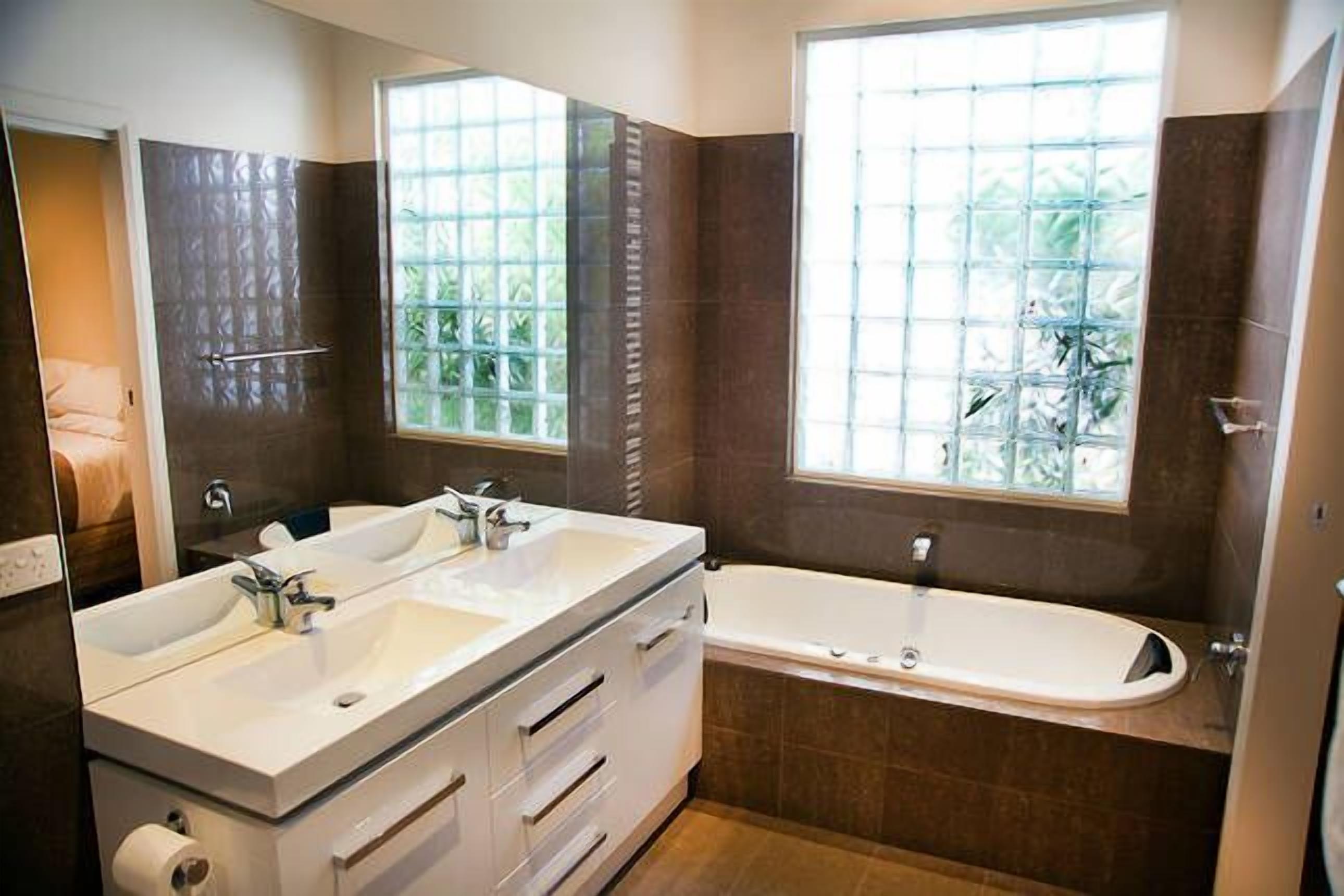A modern bathroom with a double sink vanity, a bathtub, and large windows with a view of greenery.