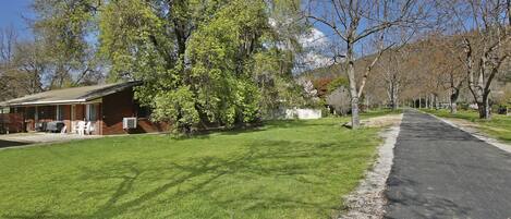 A residential area with a paved road, a grassy lawn, and a brick building with outdoor seating.
