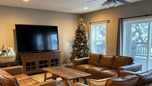 A living room with a large flat-screen TV, leather sofas, a wooden coffee table, and a Christmas tree.