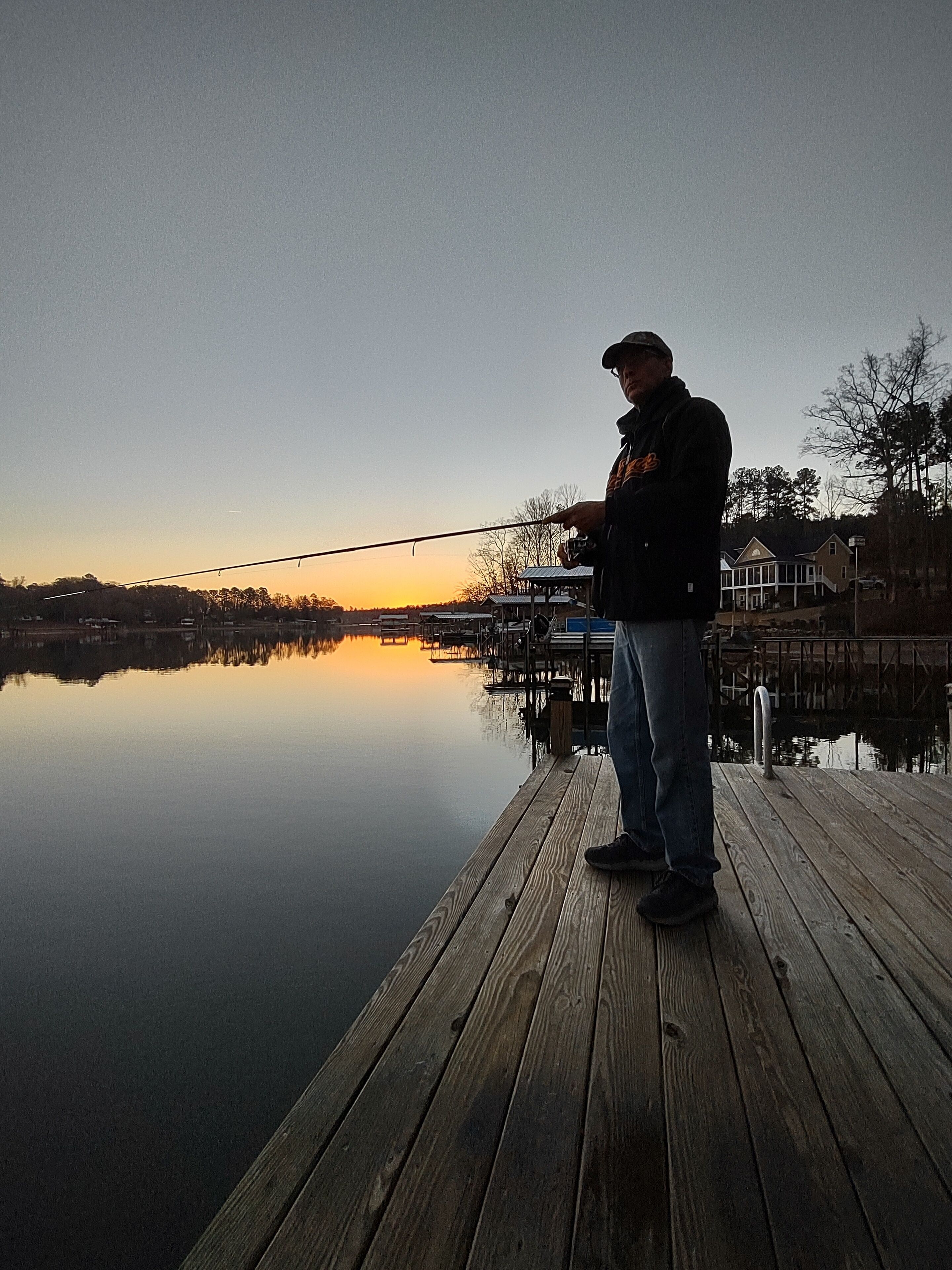 A wooden dock extending into calm water with a person fishing.