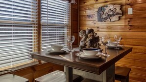 A wooden interior with a dining table set for two, a decorative wall piece, and a window with blinds. - The Nut House, Hot Tub, $560 FREE tickets each paid day (Pigeon Forge)