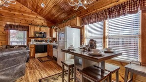 A cozy cabin interior with wooden walls and ceiling, a dining area with a table and chairs, a kitchen with appliances, and a sofa in the living area. - The Nut House, Hot Tub, $560 FREE tickets each paid day (Pigeon Forge)