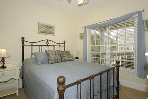 A bedroom with a bed, a nightstand, a lamp, a window with blinds, and a painting on the wall. - 15% Off, 200.00 Gift Card, 32 Crabline (Hilton Head Island)