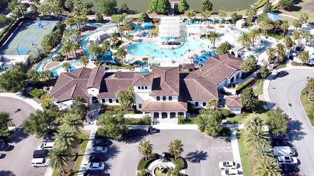 An aerial view of a resort with a swimming pool, tennis courts, and a parking area.