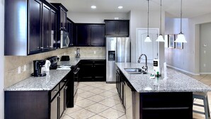 A modern kitchen with dark cabinets, granite countertops, stainless steel appliances, and pendant lighting.