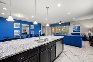 A modern kitchen with granite countertops, a built-in dishwasher, and a blue accent wall. - No Rear Neighbors • Pool & Spa • Game Room • Lazy River • Gated Resort 2167 (Kissimmee)