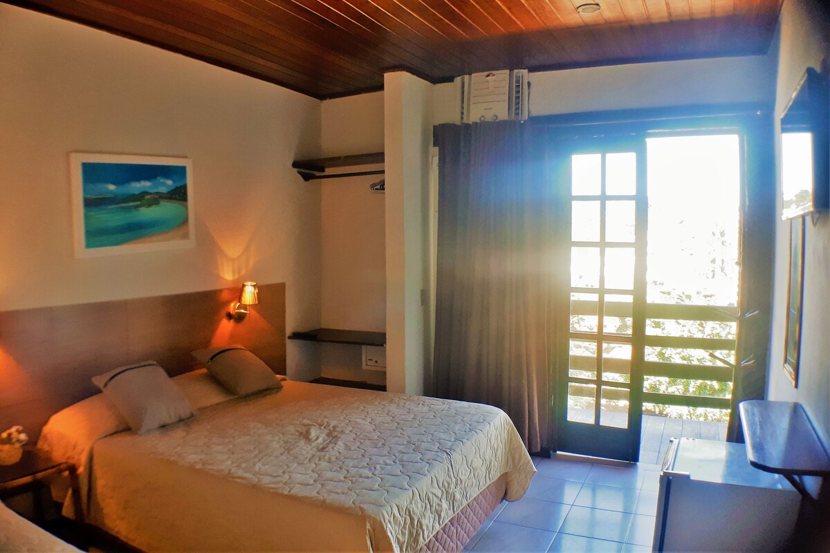 Habitación de hotel con cama, lámparas de noche, un cuadro en la pared y vistas a través de una puerta.