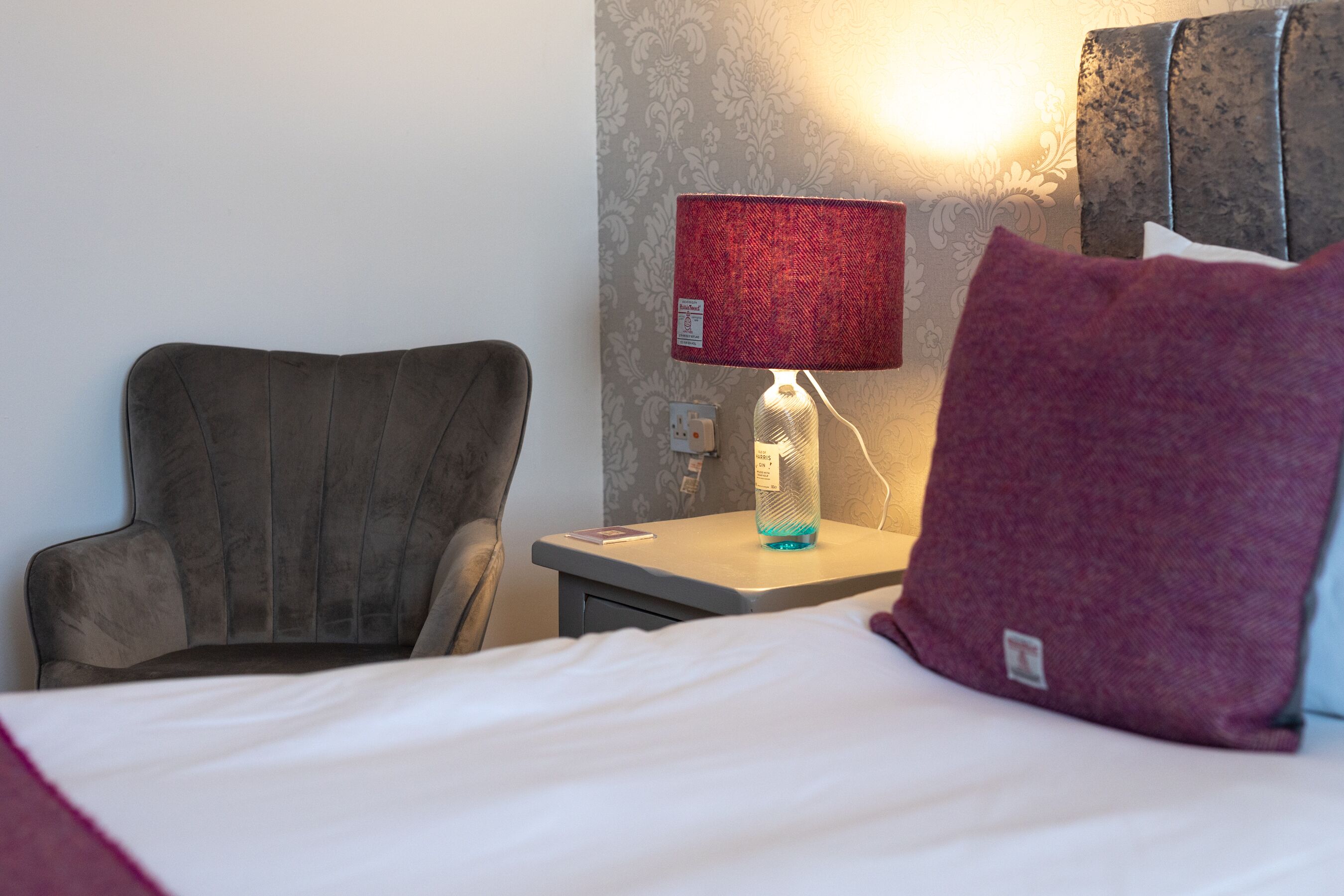 Une chambre d’hôtel comprenant un lit, une chaise, une table de chevet avec une lampe et un mur orné d’un motif texturé.
