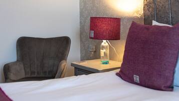 A hotel room with a bed, a chair, a nightstand with a lamp, and a wall with a textured pattern.