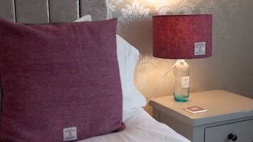 A neatly made bed with a large purple pillow, a white pillow, and a red lamp on a bedside table.