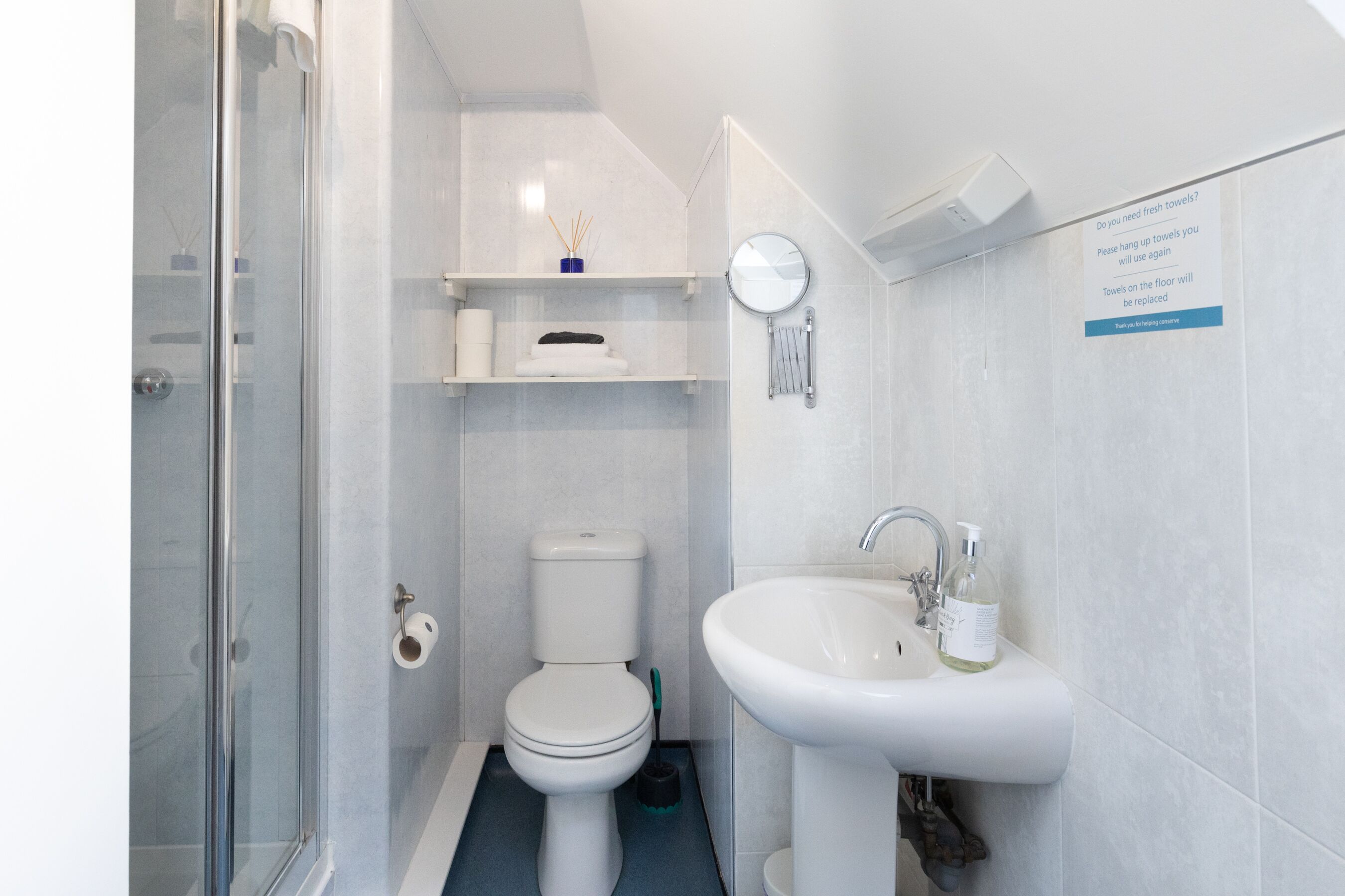 A modern bathroom with a glass shower enclosure, a toilet, a sink with a soap dispenser, and a towel rack.