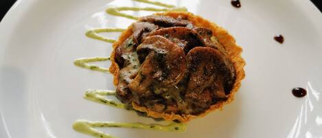 A white plate with a food item, possibly a meat-based dish, garnished with green sauce and small dark dots.