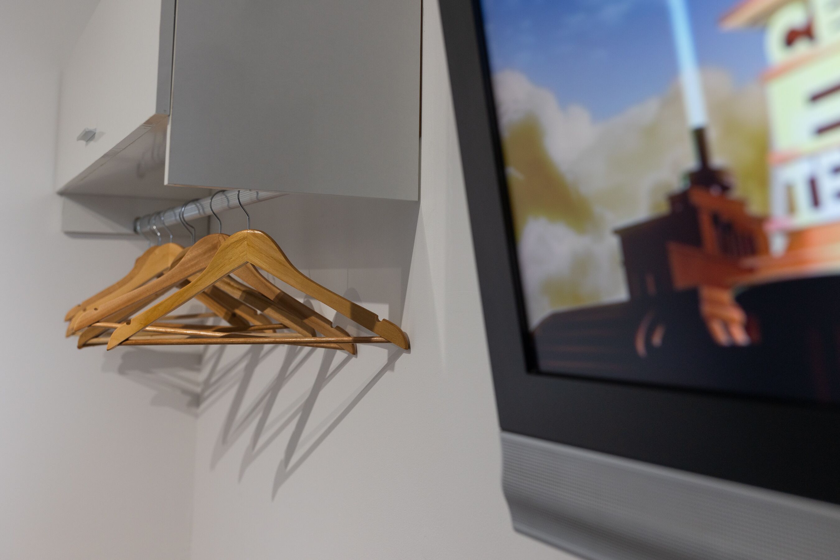 A wall-mounted wooden hanger rack with a television displaying a cityscape.