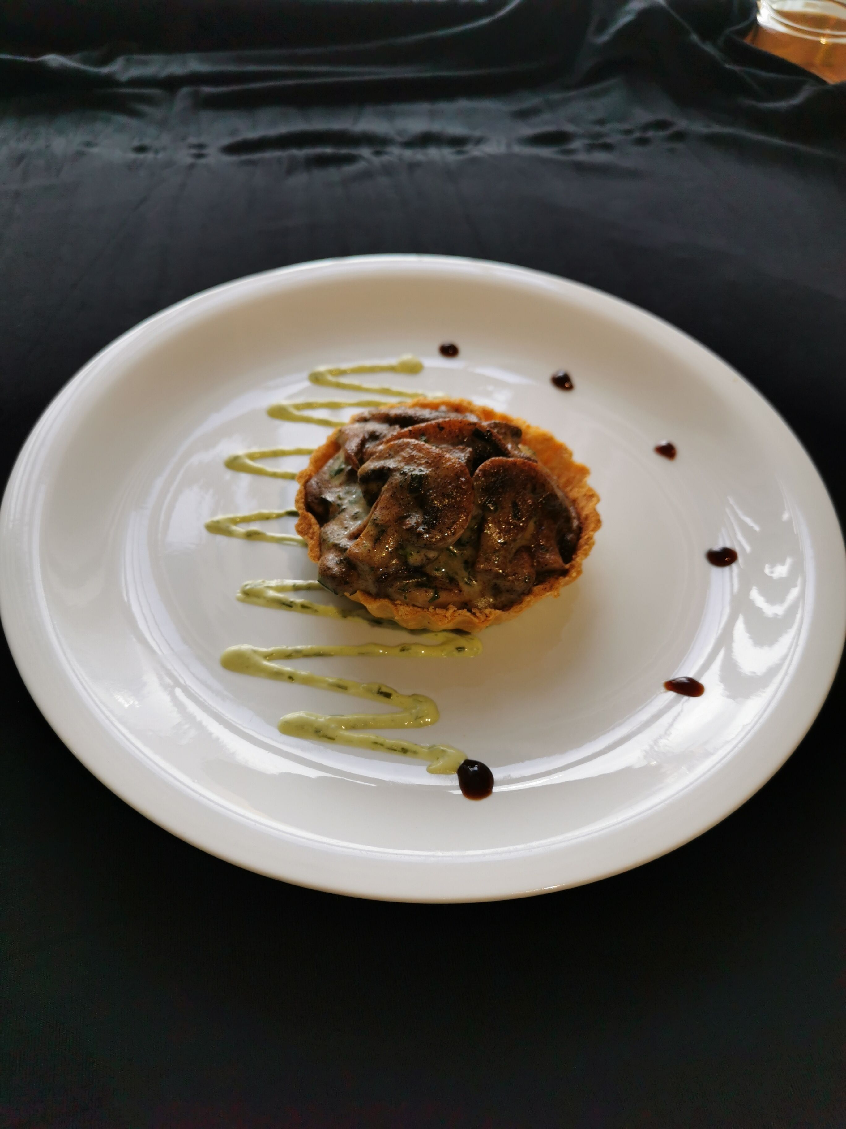 A white plate with a food item, possibly a mushroom dish, on a dark background.