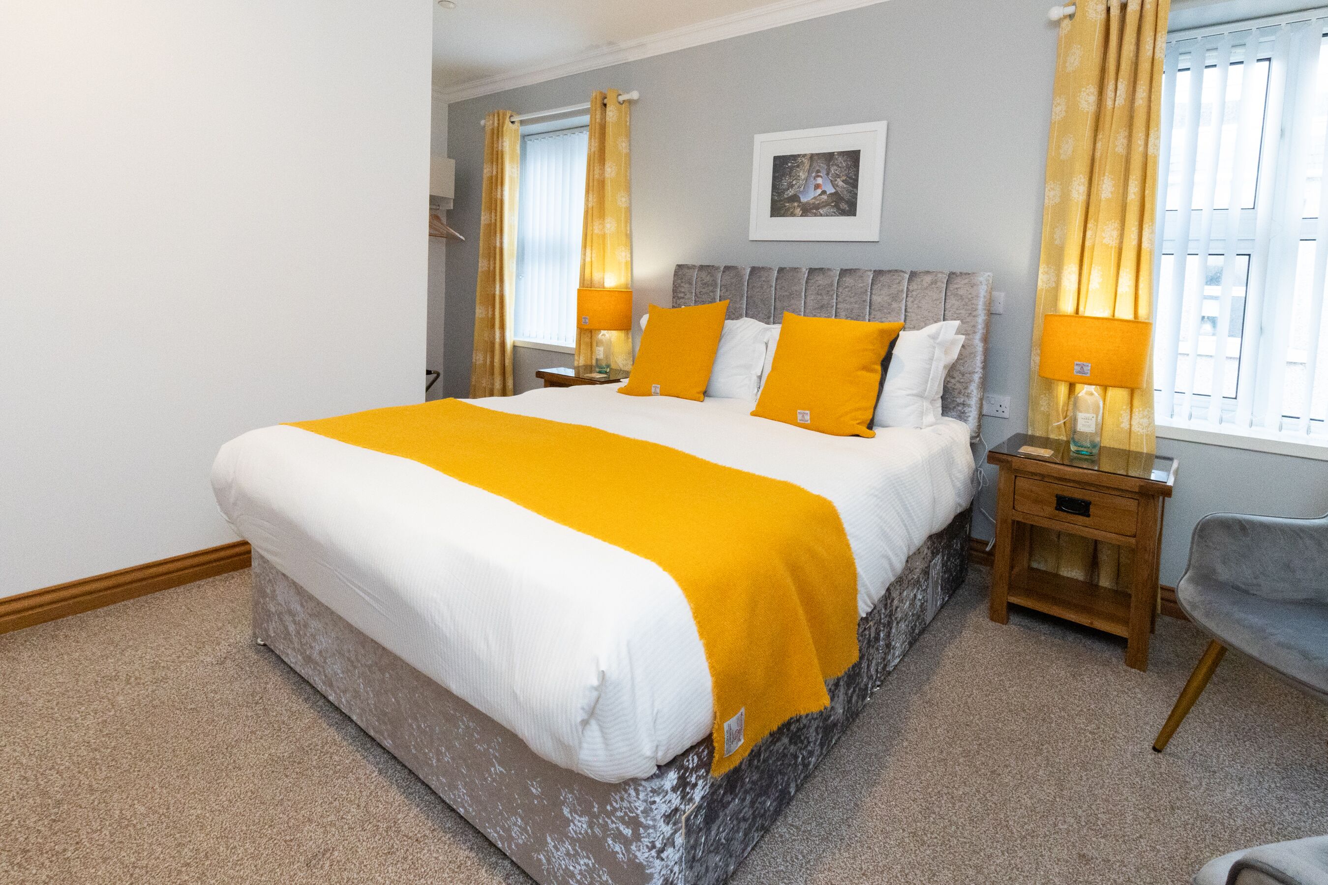 Een slaapkamer met een groot bed, twee nachtkastjes, een stoel en een raam met gordijnen.