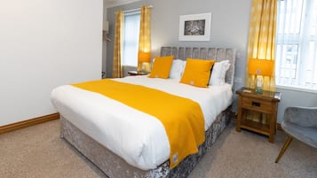 Een slaapkamer met een groot bed, twee nachtkastjes, een stoel en een raam met gordijnen.