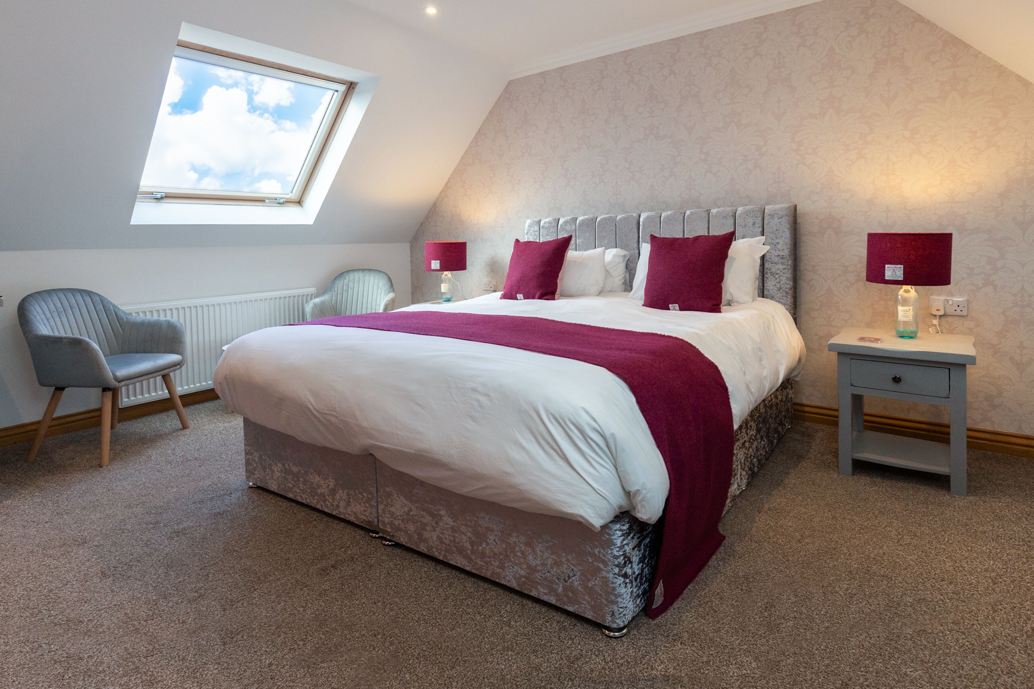 Une chambre avec un grand lit, deux tables de chevet, une chaise, une fenêtre et un radiateur.