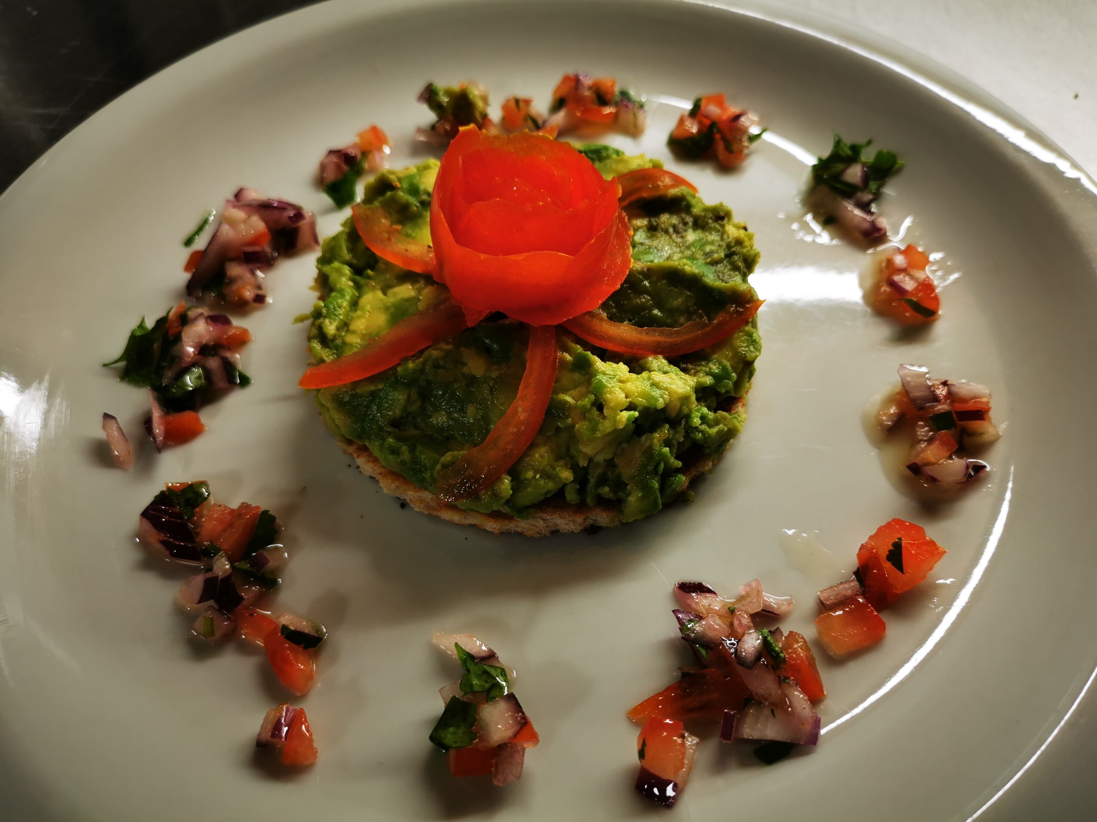 A plate with a sandwich topped with avocado, tomato, and a garnish of diced vegetables.