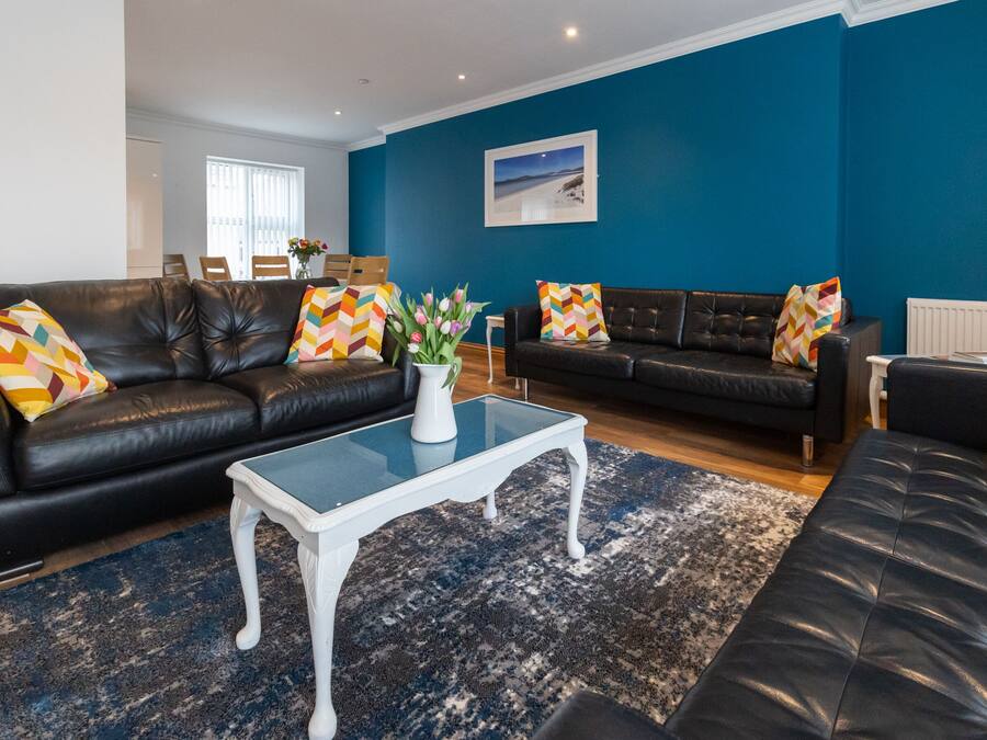 A living room with two black leather sofas, a white coffee table, and a blue wall.