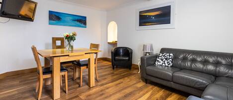A modern living room with a wooden dining table, leather sofa, and artwork on the walls.