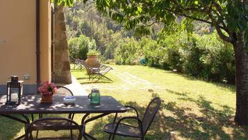 An outdoor patio with a table and chairs, surrounded by a garden and a stone wall.