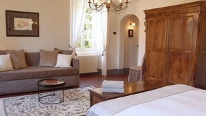 A bedroom with a bed, a sofa, a wooden wardrobe, and a window with curtains.
