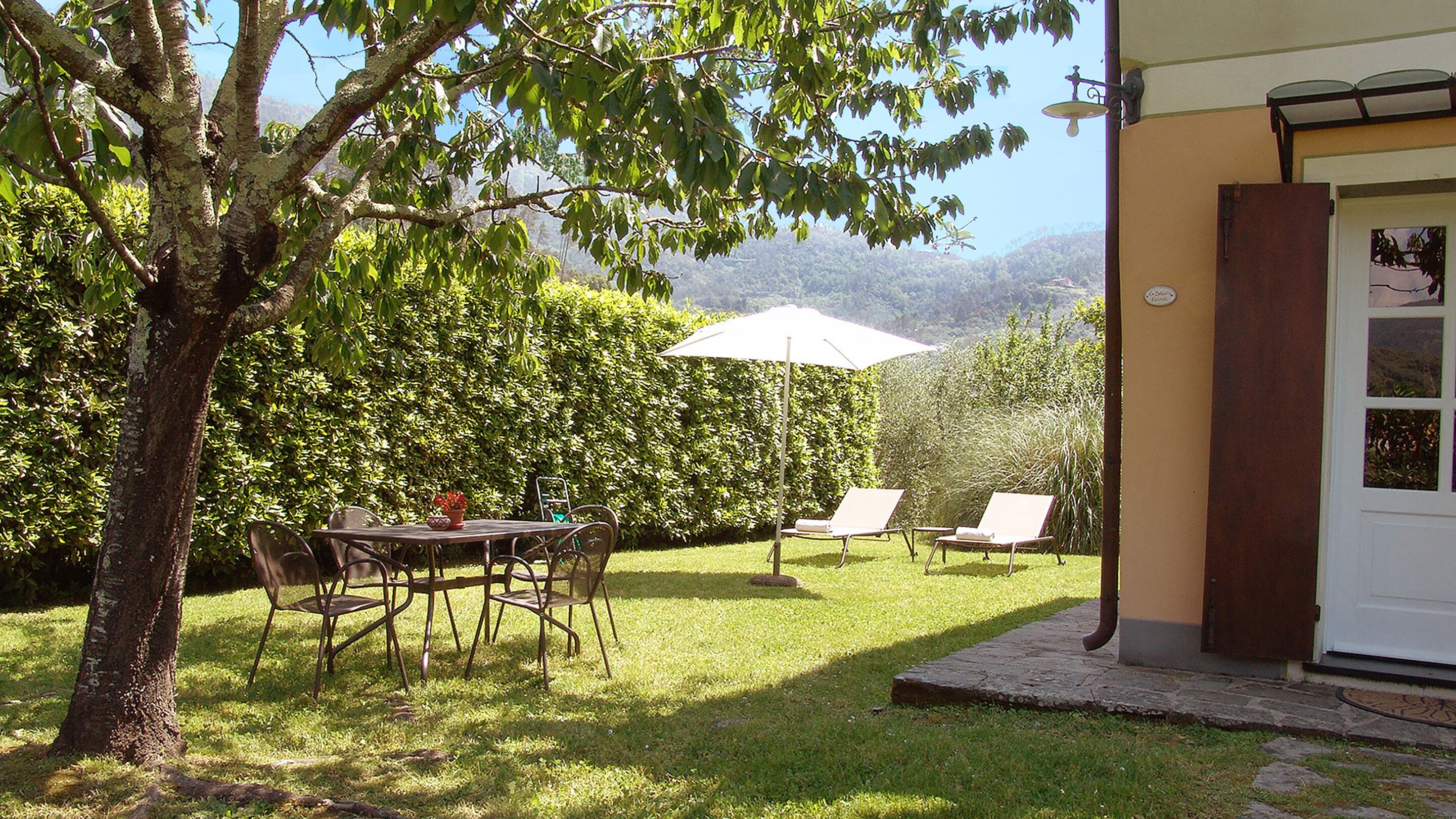 Eine Terrasse mit Tisch, Stühlen und einem weißen Sonnenschirm, sowie eine Tür zu einem Gebäude.