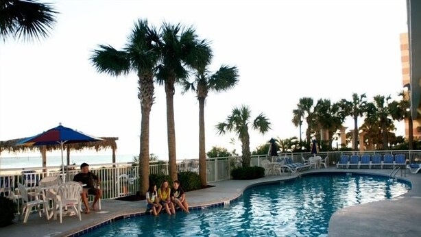 A swimming pool with palm trees, lounge chairs, and a beach view. - Gorgeous Remodeled 3BR, 2BA Camelot Oceanfront. In the heart of Myrtle Beach! (Myrtle Beach)