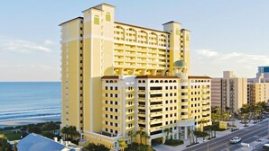 A multi-story hotel with a central courtyard, located near a beach with a clear view of the ocean. - Gorgeous Remodeled 3BR, 2BA Camelot Oceanfront. In the heart of Myrtle Beach! (Myrtle Beach)