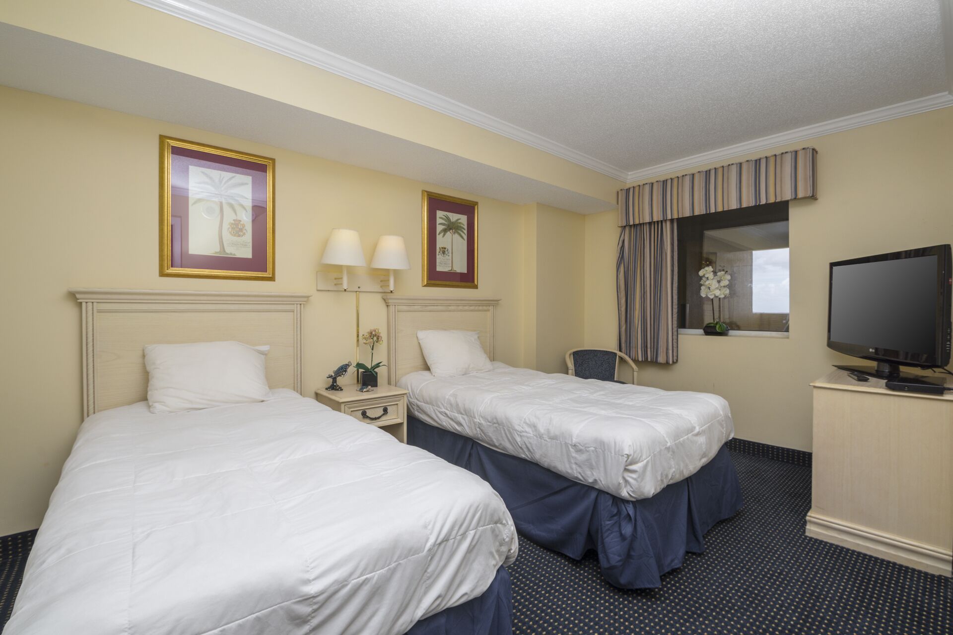 A hotel room with two beds, a desk with a television, and a window with curtains.