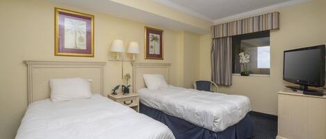 A hotel room with two beds, a desk with a television, and a window with curtains.