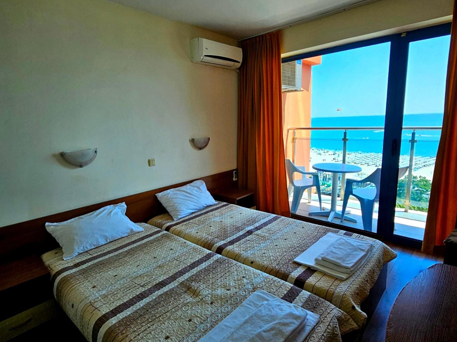 A hotel room with two beds, a balcony with a table and chairs, and a view of the beach.