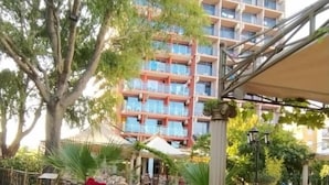 An outdoor seating area with tables and chairs, surrounded by potted plants and a building labeled "CONDOR" in the background. - Hotel Shipka Beach (Sunny Beach)