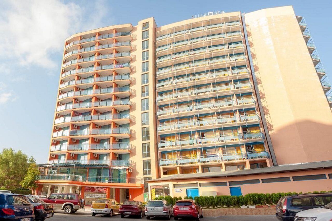 A multi-story hotel with balconies, a ground-level restaurant, and a parking area.