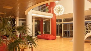 A spacious lobby with a red sofa, a palm tree, and a staircase. - Hotel Shipka Beach (Sunny Beach)