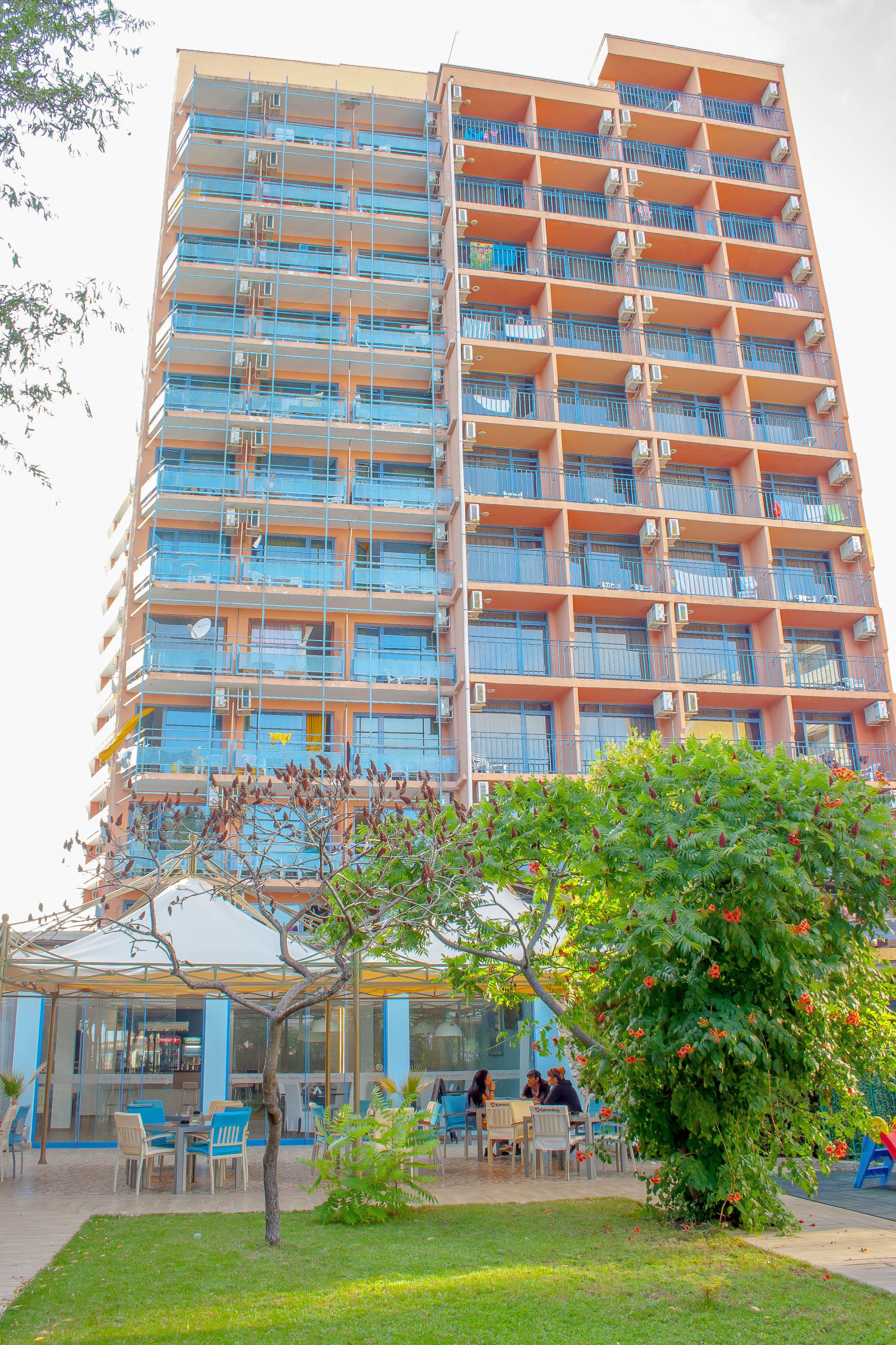 A multi-story building with balconies, a covered outdoor seating area, and a small garden.