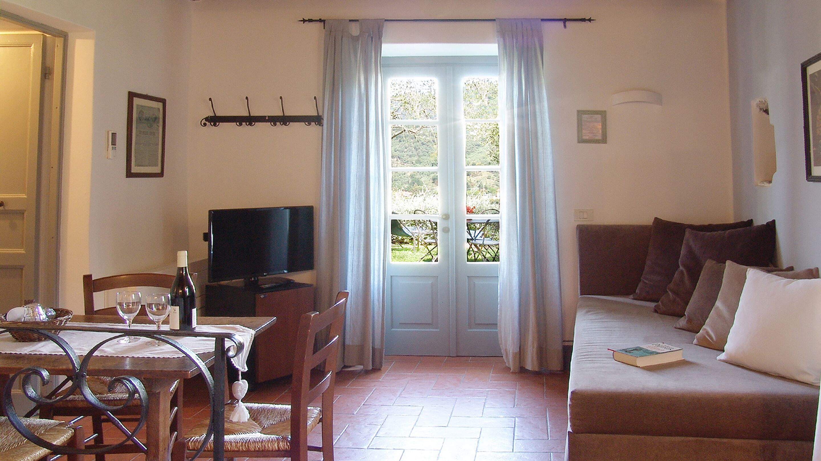Una sala de estar con televisión, una mesa de comedor con sillas, un sofá y una ventana con cortinas.