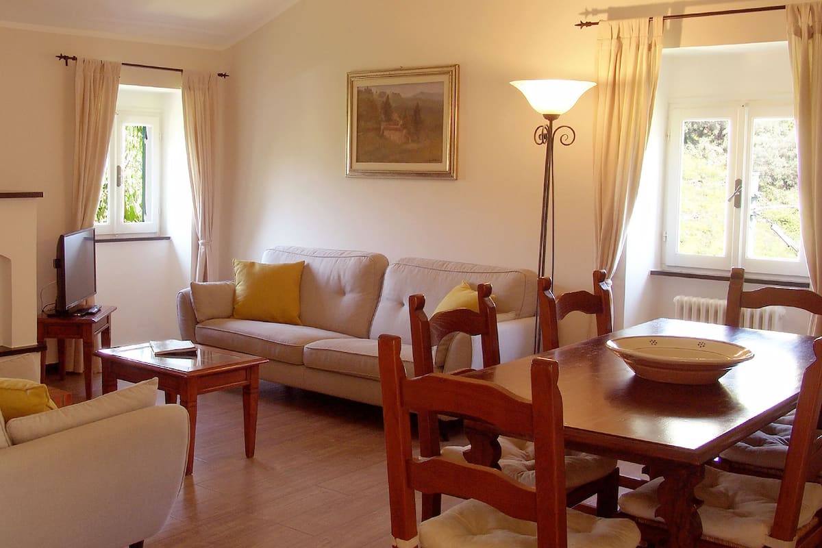 A living room with a sofa, a dining table with chairs, a television on a stand, and a painting on the wall.