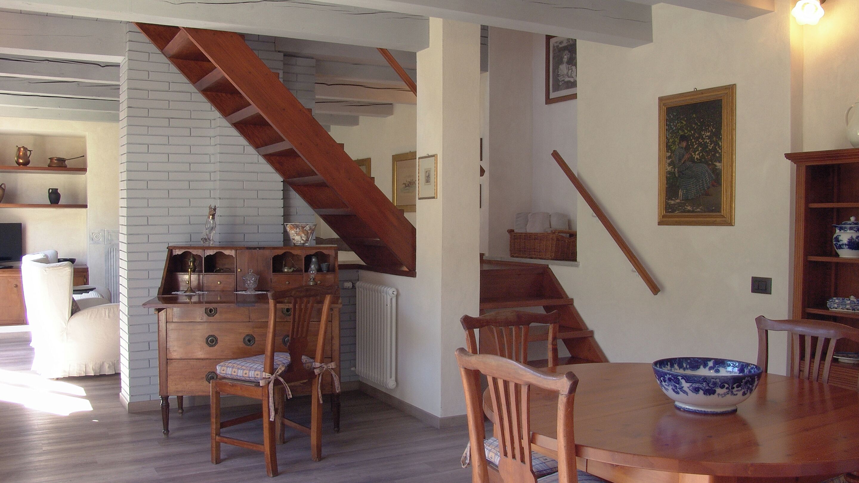 Un área de comedor con una mesa y sillas de madera, una escalera y una pared de ladrillo blanco.