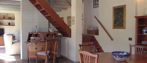 Un área de comedor con una mesa y sillas de madera, una escalera y una pared de ladrillo blanco.