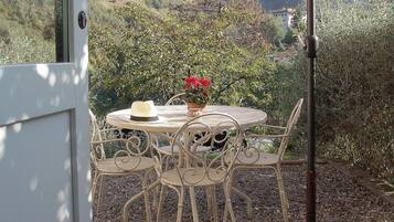 An outdoor dining area with a table and chairs under a canopy, surrounded by gravel and overlooking a mountainous landscape.