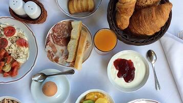 Een ontbijttafel met croissants, brood, eieren, fruit en diverse soorten beleg.