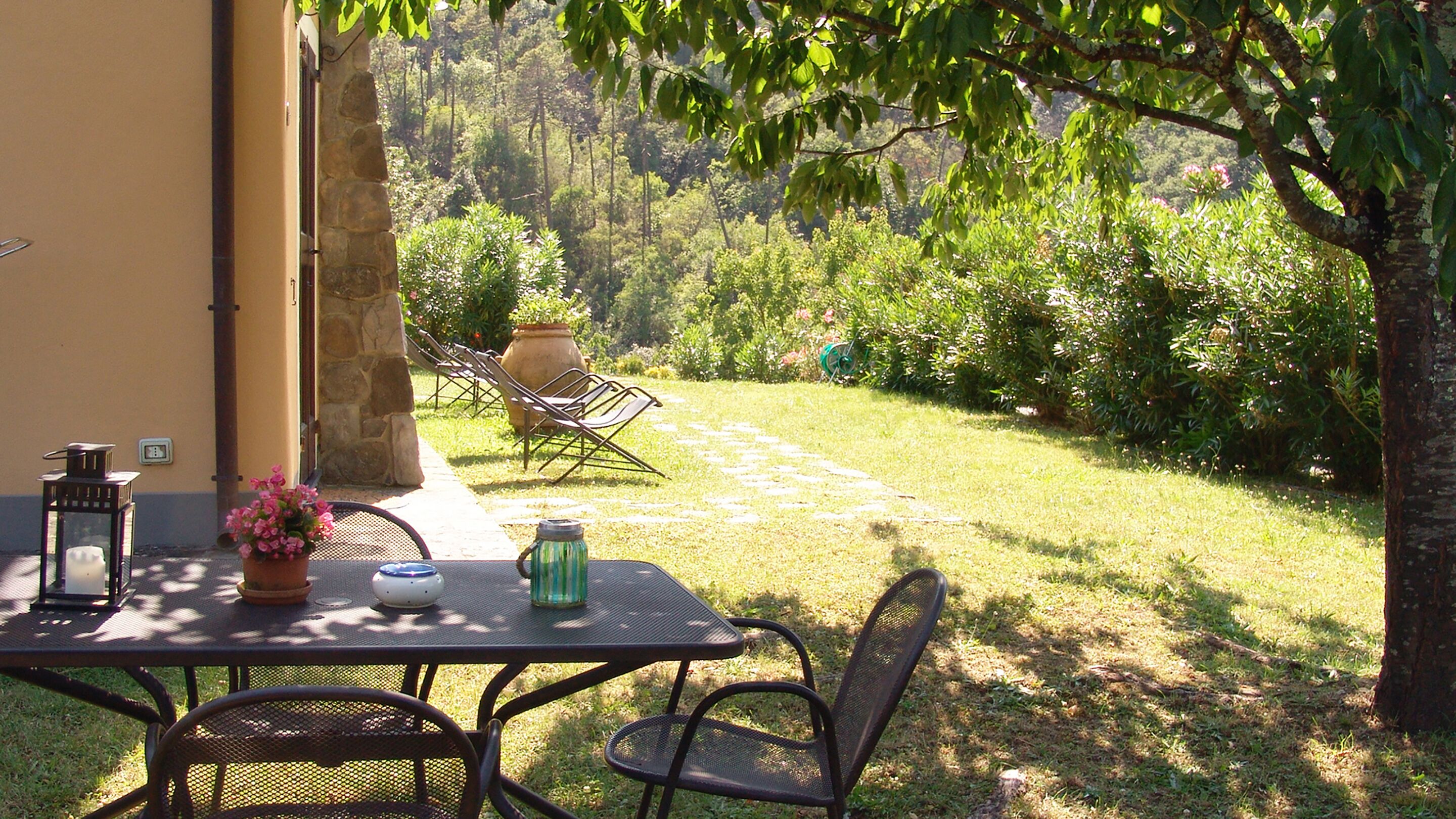 An outdoor patio with a table and chairs, surrounded by a garden and a stone wall.